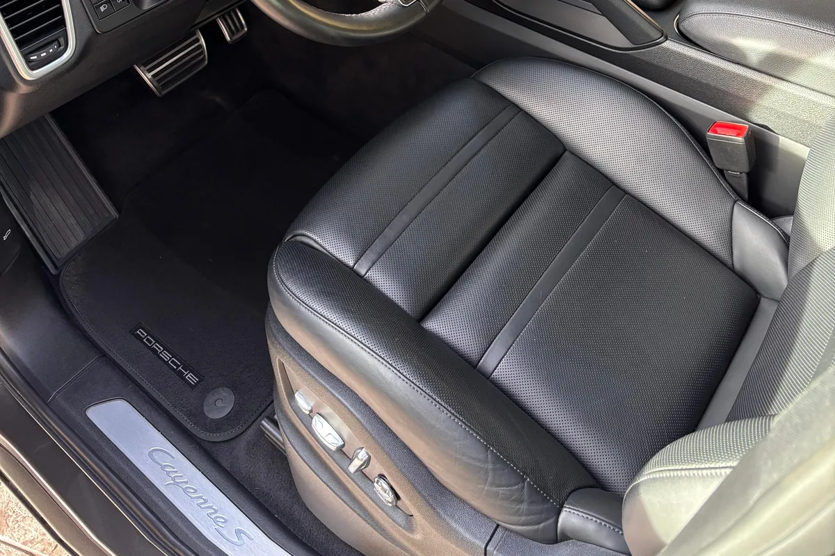 Asiento delantero de cuero negro perforado de un Porsche Cayenne S, limpio, con la alfombrilla y el umbral de la puerta en el garaje del cliente